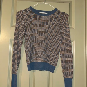 Mönstrad stickad tröja från Zara - Säljer en snygg stickad tröja från Zara med ett unikt mönster i blått och brunt. Tröjan har långa ärmar och ribbade kanter vid ärmslut och nederkant. Perfekt för att ge din outfit en cool touch!