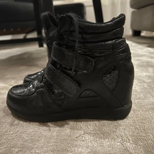 Isabel marant liknande skor - Svarta kilskor med en liten klack i, skorna har både snörning oxh karborreband på sidorna. Liknar isabel marant skorna väldigt mycket, de har en glansig yta längst fram, säljer då de var för små! Inga defekter 