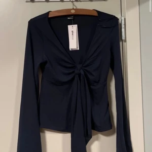 Mörkblå topp från Gina Tricot - Snygg mörkblå topp från Gina Tricot med knytning framtill och v-ringning. Toppen har långa ärmar. Ny med taggar kvar.