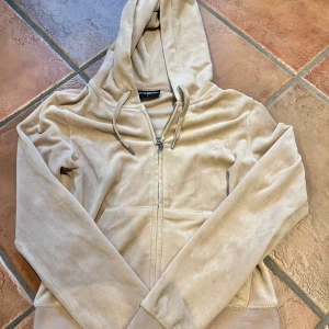 Beige hoodie från Juicy Couture - Säljer en snygg beige hoodie från Juicy Couture med dragkedja och huva. Tröjan har långa ärmar och en broderad logga på bröstet. Perfekt för en avslappnad stil. Hör av dig vid intresse! 😊