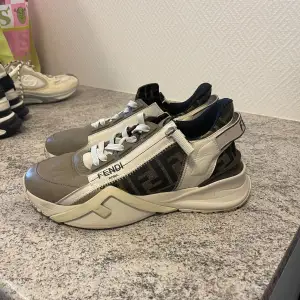 Snygga sneakers från Fendi i beige och svart med vita snören. Skorna har en unik design med Fendi-logotypen på sidan och en robust sula. Perfekta för en stilren look.