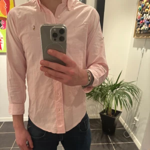 Rosa skjorta från Polo Ralph Lauren - Snygg rosa skjorta från Polo Ralph Lauren med broderad logga på bröstet. Skjortan har långa ärmar och knappar framtill. Perfekt för en stilren look.