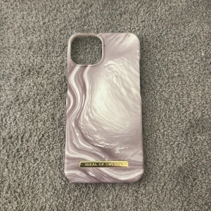 Lila mobilskal från iDeal of Sweden - Snyggt lila mobilskal från iDeal of Sweden med ett marmorerat mönster. Skalet är designat för iPhone 13 och har en elegant finish med en liten guldfärgad logotyp. Perfekt för att ge din telefon ett stilrent utseende. Aldrig använt för jag beställde fel storlek, köpt för 400kr💕