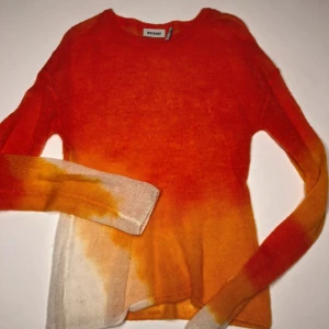 Orange och gul stickad tröja från Weekday - Säljer en cool stickad tröja från Weekday i en härlig ombre av orange och gul. Tröjan har en rund hals och långa ärmar, perfekt för att liva upp garderoben. Passar bra till både jeans och kjol. Perfekt för höst och vår! På andra bilden ser man ett litet hål i tröjan som säkert är enkelt att fixa, hålet sitter vid bröstet.