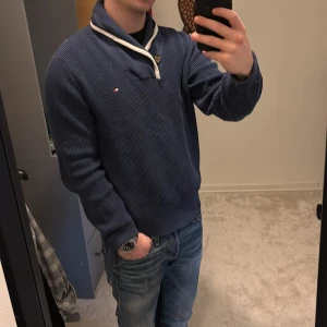 Blå stickad tröja från Tommy Hilfiger - Säljer en snygg blå stickad tröja från Tommy Hilfiger med en unik krage och knappdetalj. Tröjan har långa ärmar och en liten logotyp på bröstet. Perfekt för kyligare dagar! Skriv vid funderingar!👏🏻