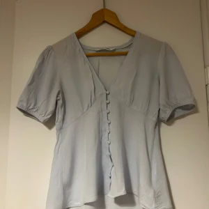 Ljusblå blus från Samsøe Samsøe - Säljer en ljusblå blus från Samsøe Samsøe med korta puffärmar och knappar framtill. Blusen har en v-ringad design! Inköpspris ca 1200 kr. 