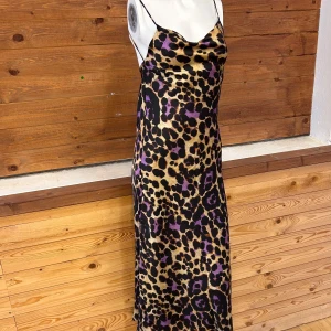 Leopardmönstrad klänning med tunna axelband - Snygg leopardmönstrad klänning med inslag av lila och guld. Klänningen har tunna axelband och en smickrande passform. Perfekt för en djärv look.