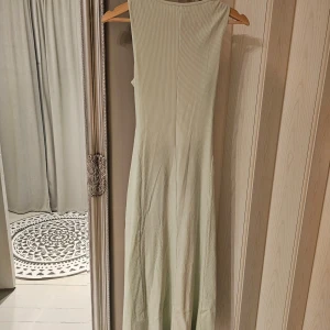 Ljusgrön ribbad långklänning med öppen rygg - OANVÄND! Snygg ljusgrön långklänning i ribbat material med en elegant öppen ryggdesign. Klänningen är ärmlös och har en lång längd som ger en stilren look. Perfekt för varma dagar eller speciella tillfällen.