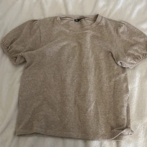 Beige t-shirt från Zara - Säljer en beige t-shirt från Zara med puffiga kortärmar. Perfekt för en avslappnad stil. Tillverkad i ett mjukt material som känns skönt mot huden.