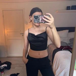 Svart satinlinne - Snygg svart satinlinne med smala axelband och en elegant  framsida. Toppen har en öppen rygg med knytband som ger en stilren look. Perfekt för fest eller andra speciella tillfällen 