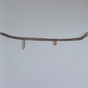 Dubbelkedjat armband med berlocker - Snyggt armband med två kedjor i silver och guldton. Armbandet har en fjäderberlock och en rund berlock som ger en bohemisk touch. Perfekt för att lägga till lite extra stil till din outfit.