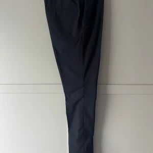 Marinblå kostymbyxor från H&M - Eleganta svarta kostymbyxor från H&M i en klassisk design. Byxorna har en rak passform och är tillverkade i en blandning av polyester och viskos för en bekväm känsla. Perfekta för en stilren look.