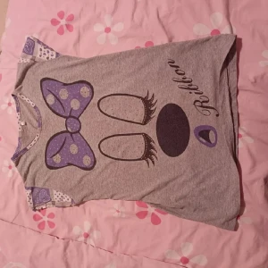 t-shirt  - Säljer en grå t-shirt med ett stort tryck av en lila prickig rosett och ögonfransar på framsidan. T-shirten har korta ärmar med lila och vita mönstrade detaljer. Perfekt för en avslappnad stil! M/S