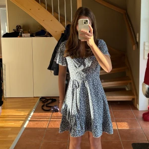 Blommig omlottklänning - Blå omlottklänning med små vita blommor. Klänningen har korta ärmar och en knytning i midjan så man kan anpassa storlek lite själv😌😌Perfekt sommar klänning.                                                 Endast använd två tre gånger💕