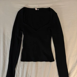 Svart ribbad topp - Snygg svart ribbad topp med långärmad design och v-ringad hals. Perfekt för en stilren look. Storleken är xxs men passar mig som brukar bära S.