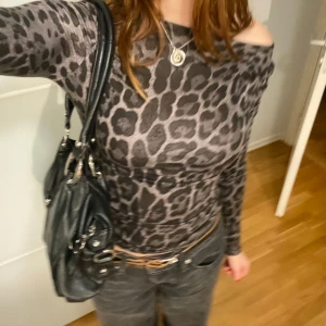Grå leopardmönstrad offshoulder topp - Snygg grå leopardmönstrad topp med offshoulder-design och långa ärmar. Perfekt för en trendig look. Klippte vid urringningen för att kunna ha den off shoulder. Det varken syns eller sprettas upp. 