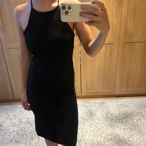 Svart ribbad klänning - Snygg svart ribbad klänning med smala axelband och en tight passform. Perfekt för en stilren look. Klänningen är knälång och har en enkel design som gör den lätt att matcha med olika accessoarer.