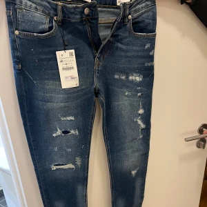 Blå skinny jeans från Zara - Snygga blå skinny jeans från Zara med slitna detaljer och en modern look. De har en klassisk femficksdesign och är perfekta för en trendig stil. Midjan är midwaist och de har en dragkedja och knapp framtill.