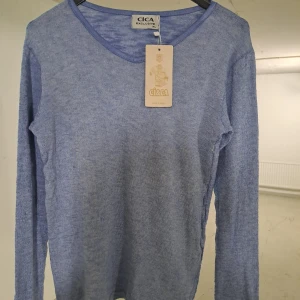 Blå långärmad tröja från Cica - Säljer en stilren blå långärmad tröja från Cica. Tröjan har en enkel design med rund hals och är perfekt för en avslappnad look. Passar bra till jeans eller kjol för en casual stil.