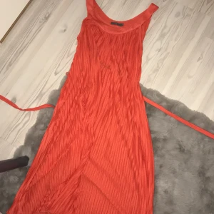 Orange ärmlös klänning från FFK - Snygg orange ärmlös klänning från FFK. Klänningen är ärmlös, enkel, lös och luftig. Den har även ett skjutbana runt midjan. Inga fläckar eller så.