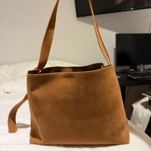 Brun axelväska i mocka - Snygg brun axelväska i mocka med justerbart bälte. B36 H27. Köpt på en dansk företag Design by si