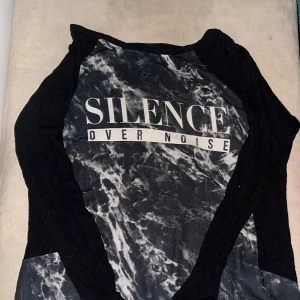 Svart och grå långärmad tröja från Gina Tricot - Säljer en cool svart och grå långärmad tröja från Gina Tricot med texten 'Silence Over Noise' på framsidan. Tröjan har ett marmorerat mönster och är perfekt för en avslappnad stil.