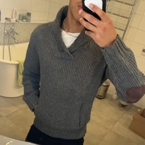 Grå stickad tröja från H&M L.O.G.G. - Säljer en stilren grå stickad tröja från H&M L.O.G.G. med en snygg krage. Perfekt för kyliga dagar och ger en avslappnad look. 