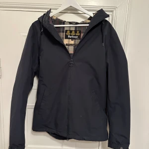 Barbour Jacka - Snygg jacka från Barbour. Jackan har dragkedja och huva, perfekt för höst och vår. Hör av dig vid frågor!