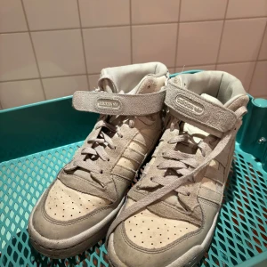 Beiga Adidas sneakers  - Säljer ett par beiga sneakers från Adidas med hög modell och snörning. Skorna har även en praktisk kardborreband för extra stöd. 