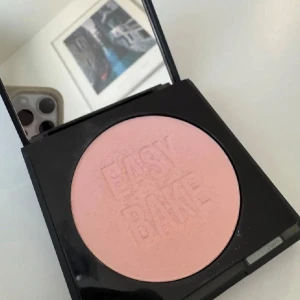 HUDA BEAUTY - Easy Bake puder - Ett puder i en ljusrosa nyans från Easy Bake. Kommer i en fyrkantig svart dosa med spegel i locket. Perfekt för att sätta sminket och ge en matt finish.