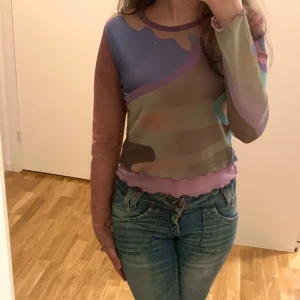 Flerfärgad meshtröja - Säljer en cool flerfärgad meshtröja. Tröjan har ett abstrakt mönster i lila, blått, grönt och beige. Den är långärmad och har en croppad passform med vågig kant nedtill. Perfekt för att ge din outfit en unik touch! Använd ett fåtal gånger, gott skick! 💗