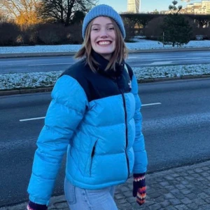 Blå pufferjacka från The North Face - Säljer en snygg blå pufferjacka från The North Face med svart axelparti och dragkedja. Jackan har en hög krage och två sidofickor med dragkedjor. Perfekt för kyliga dagar. Kvinna storlek S. Kan mötas upp i Malmö. Kan skickas men då står köparen för frakten. 