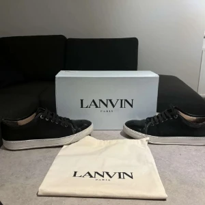 Svarta sneakers från Lanvin - Säljer ett par stilrena svarta sneakers från Lanvin i mycket bra skick. Skorna har en snygg svart ovandel med snörning och en vit sula som ger en cool kontrast. Perfekta för både vardag och festliga tillfällen!