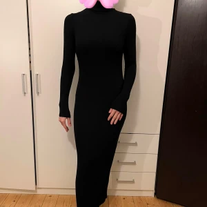 Svart långklänning med polokrage - Snygg svart långklänning med polokrage och långärmad design. Perfekt för höst och vinter, den är både elegant och bekväm. Klänningen har en tight passform som framhäver figuren. Perfekt för både vardag och festliga tillfällen!