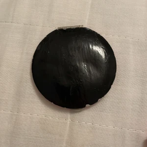 Rund fickspegel i rött och svart - Snygg och praktisk rund fickspegel med ett stilrent rött och svart yttre. Perfekt att ha med i väskan för snabba touch-ups under dagen. Spegeln är lätt att öppna och stänga med ett enkelt gångjärn.