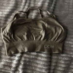 Olivgrön sporttopp från Drop of Mindfulness - Snygg olivgrön sporttopp från Drop of Mindfulness med ribbad nederkant och smala axelband. Perfekt för träning och ger bra stöd. Stilren design med logga framtill. Ni står för frakt 