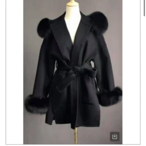 Svart kappa med pälsdetaljer - Snygg svart kappa med fluffiga pälsdetaljer på krage och ärmslut. Den har ett knytbälte i midjan för en elegant passform. Perfekt för höst och vinter när du vill hålla dig varm och stilren. 🖤