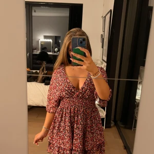 Blommig klänning med v-ringning - Säljer en superfin blommig klänning med v-ringning och trekvartsärm. Den har en härlig passform med omlott-detalj i midjan som ger en smickrande siluett. Perfekt för vår och sommar! 🌸