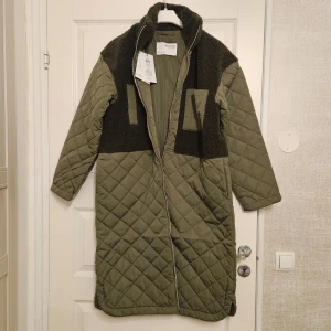 quiltad kappa från Selected Femme - Säljer en olivgrön quiltad kappa från Selected Femme med teddy-detaljer på axlar och bröst. Jackan har en dragkedja framtill och långa ärmar. Helt ny,  prislappen sitter kvar!