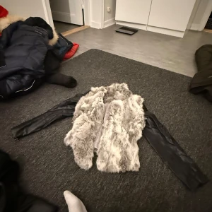 Grå pälsjacka med skinnärmar från Hollies - Snygg grå pälsjacka från Hollies med svarta skinnärmar. Perfekt för att hålla sig varm och stilren under kyliga dagar. Jackan har en lyxig känsla med sin kombination av material och färger.