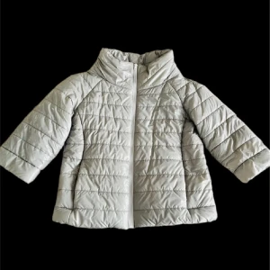 Ljusgrå quiltad jacka - Snygg ljusgrå quiltad jacka med dragkedja och hög krage. Perfekt för kyliga dagar med sin pufferdesign som håller dig varm. Jackan har trekvartsärmar och en stilren look.