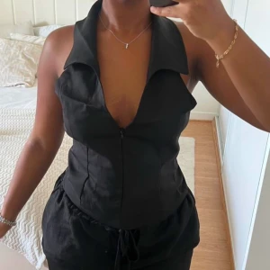 Svart korsettväst - Snygg svart korsettväst med dragkedja fram. Perfekt för en festlig kväll eller som ett stilrent tillskott till din garderob. Västen har en v-ringad design och ger en tight passform som framhäver figuren.