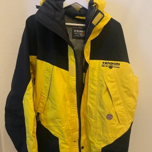 Gul och svart jacka från Tenson - Säljer en cool gul och svart jacka från Tenson i storlek XL. Den är gjord av polyester och har Gore-Tex teknologi för att hålla dig torr. Perfekt för utomhusaktiviteter med dragkedja och flera fickor. Jackan är i bra skick och redo för nya äventyr!