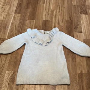 Vit stickad tröja från H&M - Söt vit stickad tröja från H&M med volangdetalj runt halsen. Perfekt för de kallare månaderna. Tröjan har långa ärmar och en knapp i nacken för enkel påklädning.