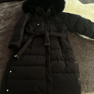 Svart dunjacka från MaxMara - Snygg svart dunjacka från MaxMara med huva och bälte i midjan. Jackan har långa ärmar och knappar längs sidorna. Den är helt ny, vilket innebär att jag aldrig har använt den. hör av er vid intresse eller fler bilder, pris kan diskuteras💞💞