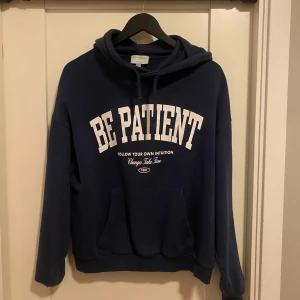 Mörkblå hoodie med text - Säljer en mörkblå hoodie med texten 'BE PATIENT' i vitt på framsidan. Säljer för den är för liten. Skriv för mer frågor