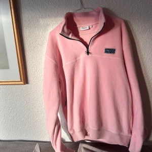 Rosa fleece tröja från Patagonia - Mysig rosa fleece tröja från Patagonia med halv dragkedja och broderad logga på bröstet. Perfekt för kyliga dagar med sin mjuka och varma känsla. 