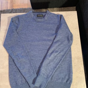 Blå tröja från Bruun & Stengade i färgen melijerad blå, materialet är fin ull och lite merino ull, storleken är S/XS - Säljer en snygg melijerad blå tröja från Bruun & Stengade i storlek S/XS, matrijalet på tröjan är fin ull och lite merinoull, tröjan är jätte bekväm nu till vintern men har ett pytte pytte litet håll i arm Hållan som knappt syns, kom med frågor med mera