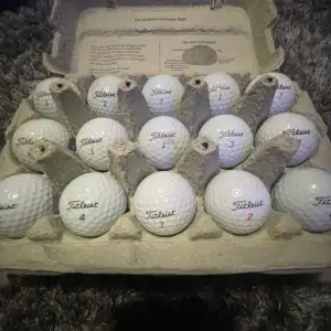 Säljer ett set med golfbollar från Titleist, förpackade i en äggkartong. Perfekt för golfentusiasten som vill ha högkvalitativa bollar för nästa runda. Bollarna är vita och numrerade för enkel identifiering på banan.