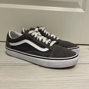 Gråa Vans sneakers - Säljer ett par gråa Vans sneakers i mocka med klassisk vit sula och snörning. De har den ikoniska vita sidostripen och är i mycket bra skick. Perfekta för vardagsbruk och ger en skön streetstyle-look. Storlek 42, nypris:850 vårt pris 600